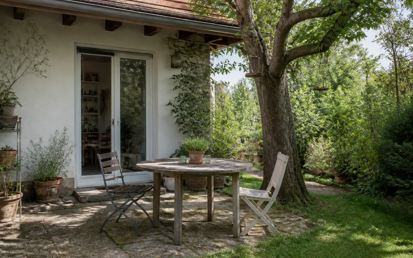 Geschützter Gartenplatz mit Holztisch, Stühlen, Obstbaum und Gartentür an einem österreichischen Wohnhaus